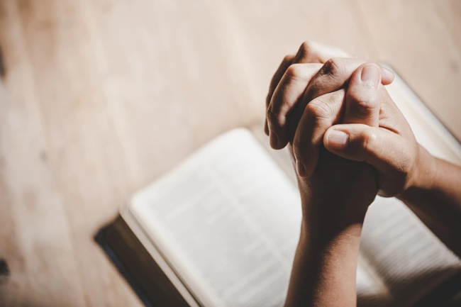 A person with folded hands in a gesture of prayer as a meditation. The image depicts a person, whose gender and specific features are not discernible, holding their hands together in a reverent manner.