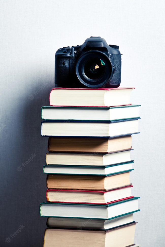 A visually appealing arrangement of books and a camera. The books are stacked on top of each other, forming a small tower, with the camera placed on the top. The books are varied in size, color, and thickness, suggesting a diverse range of topics and genres and a big help in meditation.