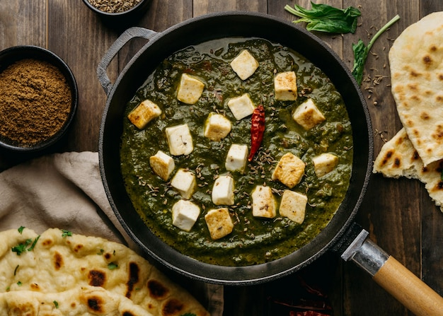 An appetizing photograph showcasing a plate of Palak Paneer and freshly baked Naan. The plate contains a generous serving of Palak Paneer, a creamy spinach-based curry with cubes of paneer (Indian cottage cheese) nestled within. The vibrant green color of the curry is visually appealing and indicative of the nutritious spinach used in its preparation. 