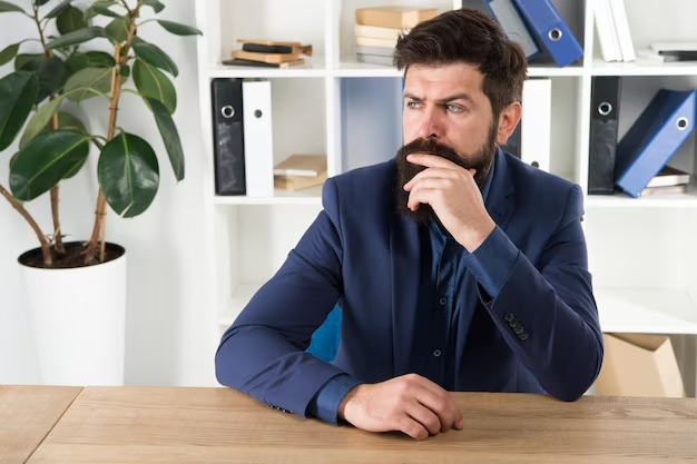 A young man, a solopreneur, is depicted in his office, lost in deep thoughts, with a pensive expression on his face. The image conveys a sense of self-doubt and imposter syndrome, highlighting the internal struggles and uncertainties experienced by individuals in their entrepreneurial journey.