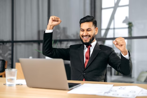 A professional person, dressed in business attire, celebrating their success by raising their hand up high in the sky. The person's face is beaming with joy and accomplishment. 